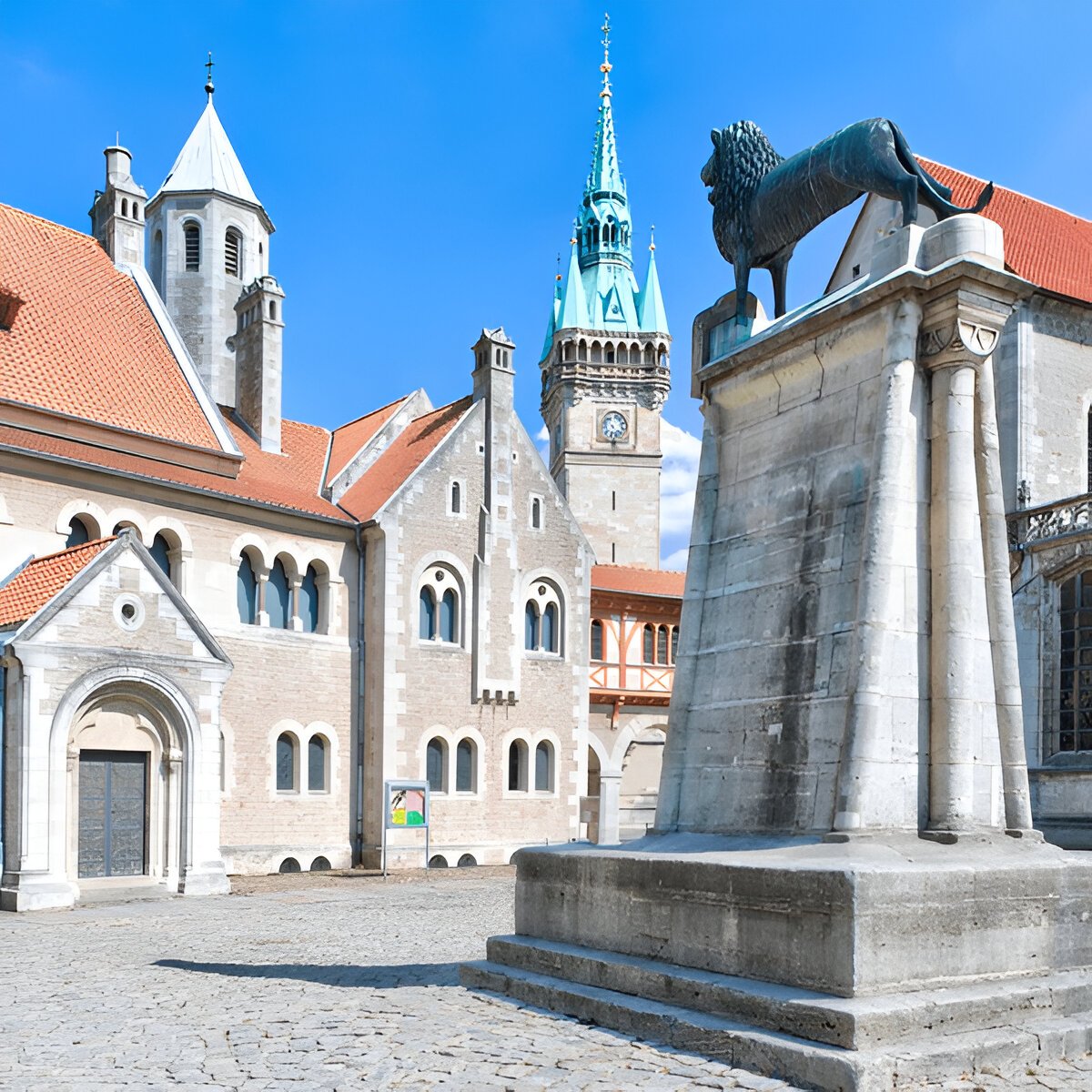 Bronze lion statue on a tall stone pedestal in a medieval square with church towers behind