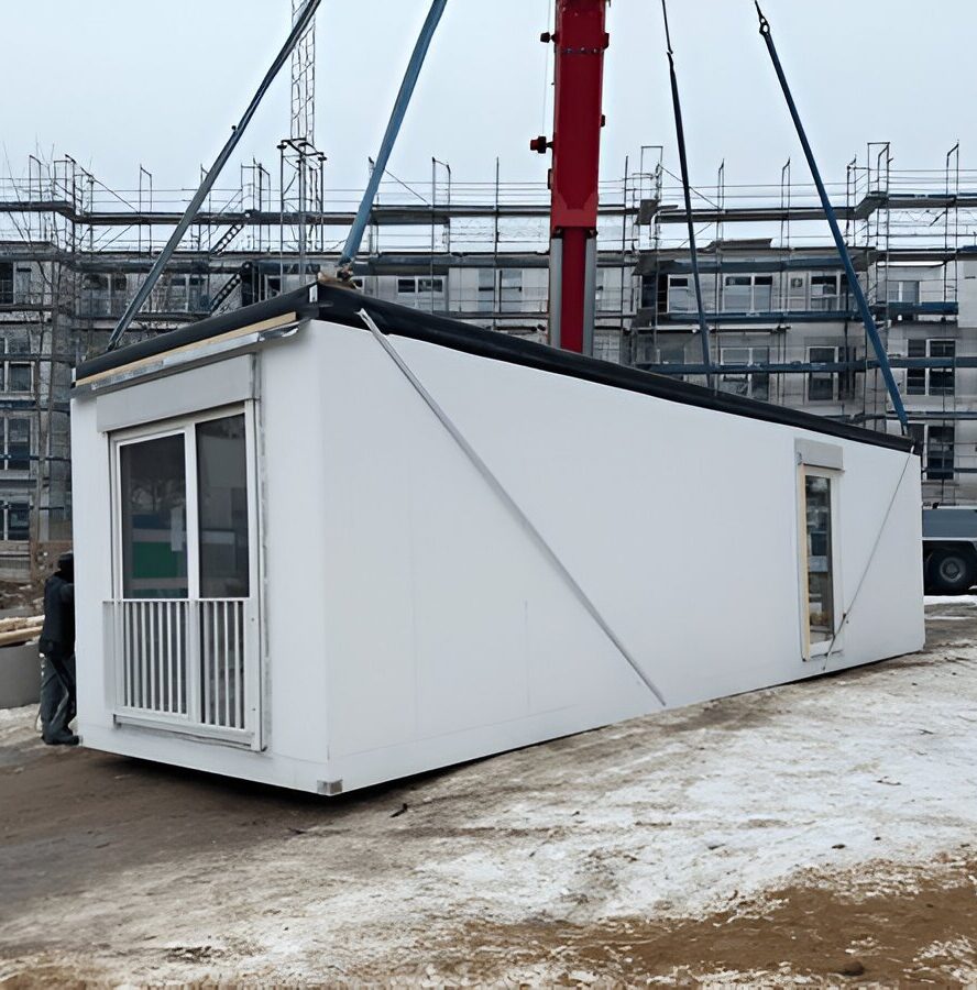 Prefab modular site cabin being lifted by crane straps at a snowy construction site