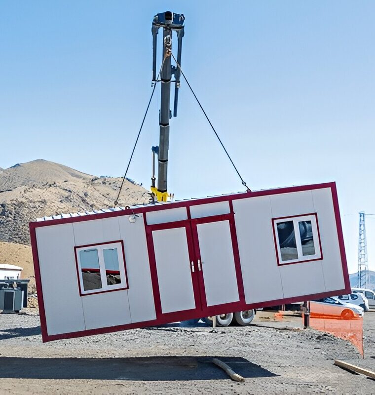 Crane lifting a prefabricated modular cabin at a construction site in a desert mountain area