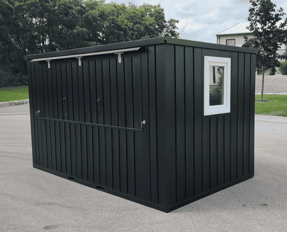 Black flat-pack container shed with vertical steel cladding and a white window, on a paved lot