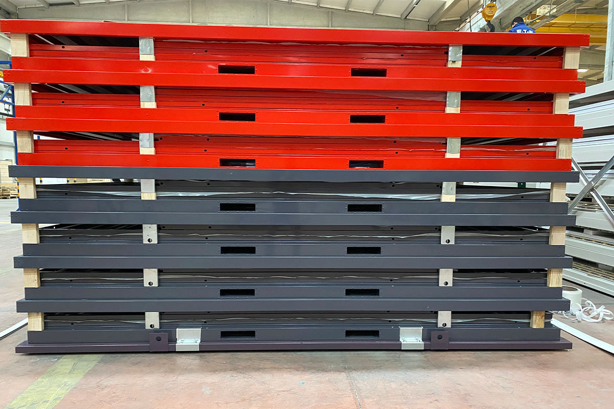 Stack of red and charcoal flat-pack container frames on pallets in a warehouse, ready for delivery