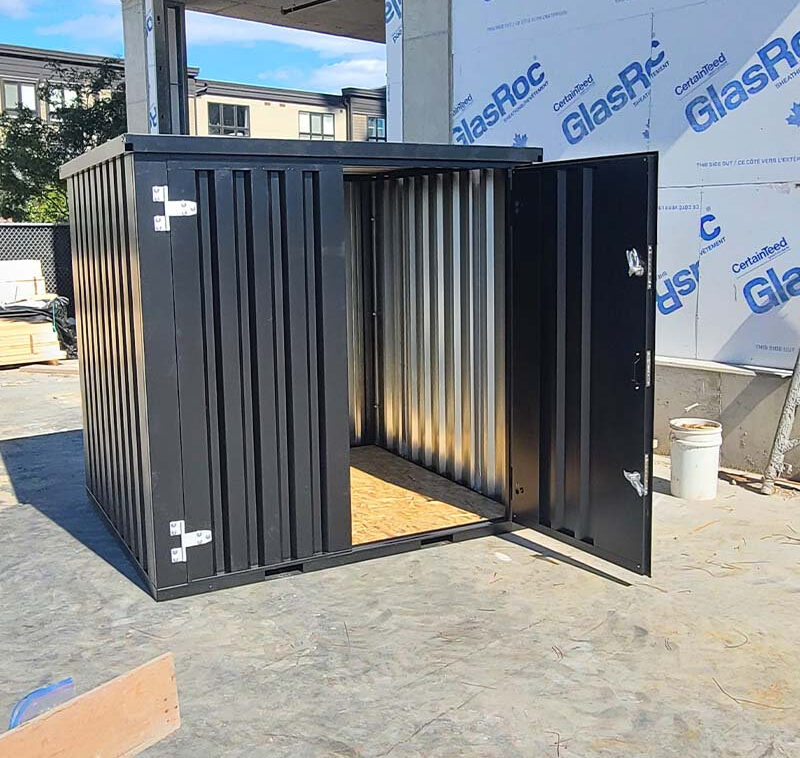 Dark-grey steel storage container with double doors open on a construction site, showing the plywood floor and corrugated walls